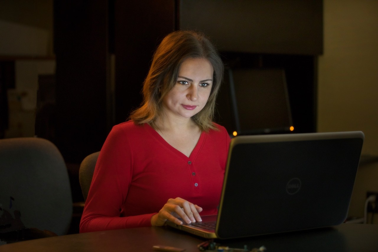 Dr. Nelly Elsayed is sitting in a dark room, with the light of her open laptop illuminating her face