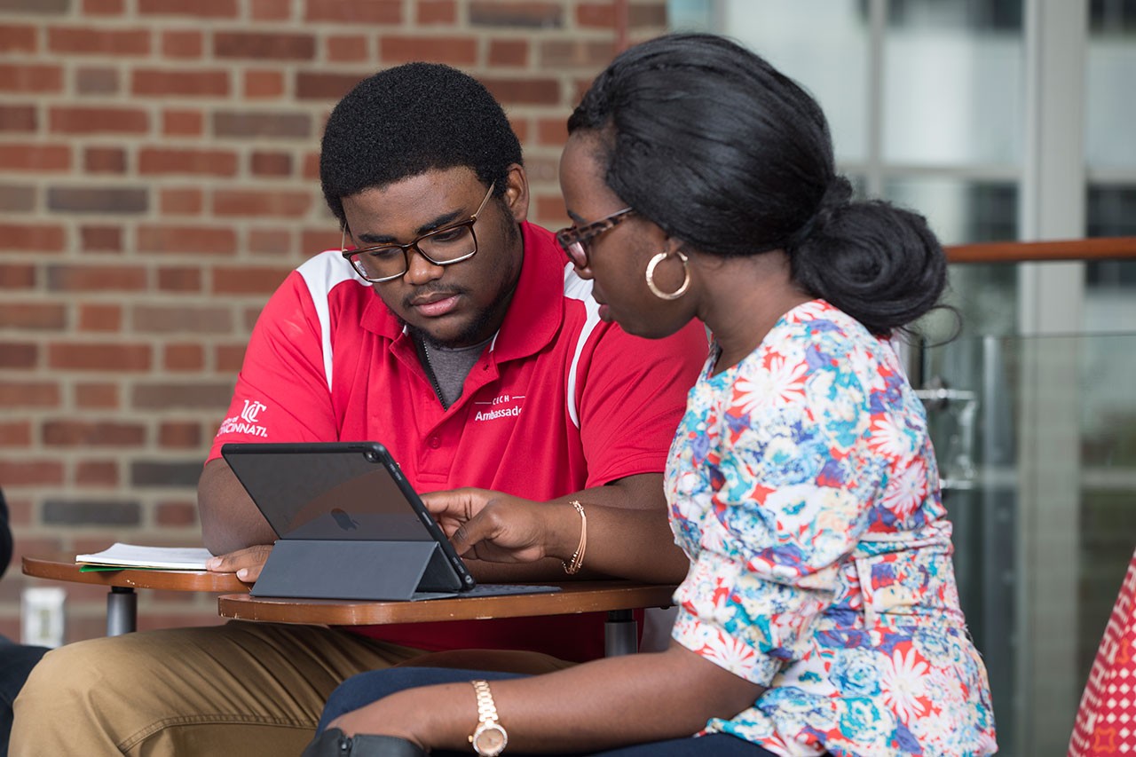 Photo of two students sitting and talking around a laptop computer 